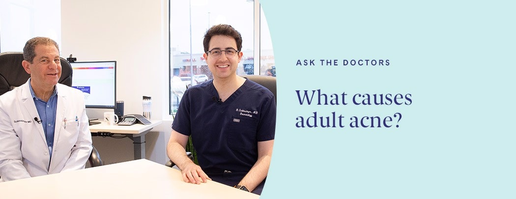 Two dermatologists, one with fair skin and dark hair wearing a dark blue shirt and one with light hair wearing a white jacket, smile at the camera.