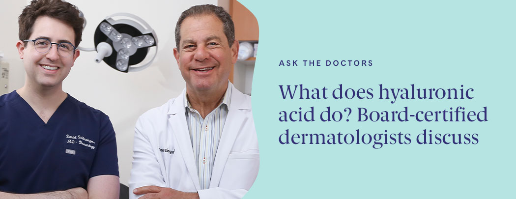 Two dermatologist, one in his 30s with fair skin & dark hair & one in his 60s with light brown hair smile while crossing their arms.