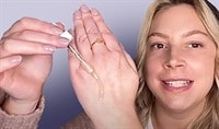 A blond woman smiling and dropping serum onto the top of her hand.