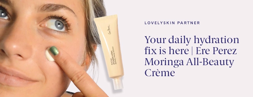 A woman with fair skin and blue eyes presses a dollop of Ere Perez Moringa All Beauty Cream into her cheek.