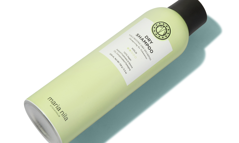 A hand holding a bottle of dry shampoo