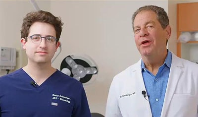 Two dermatologists stand in a clinic room next to one another.