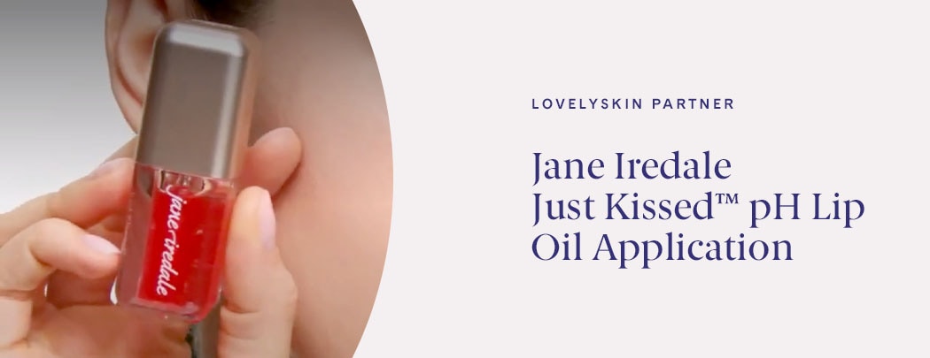 A person with fair skin holds a tube of Jane Iredale Just Kissed pH Lip Oil next to their cheek.