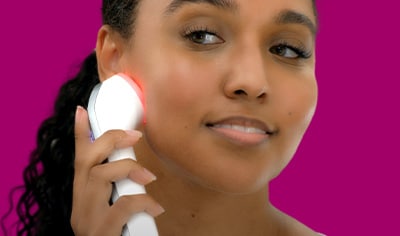 A woman with a deep skin tone and curled dark brown hair pulled into a low ponytail presses the Althaea Skin CARA Multi-Modal Tool to her face.