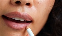 A person with a medium skin tone places an Ere Perez Acai Lip Pencil to their lip.