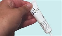 A hand holding a tube of Glo Skin Beauty Acne Spot Treatment