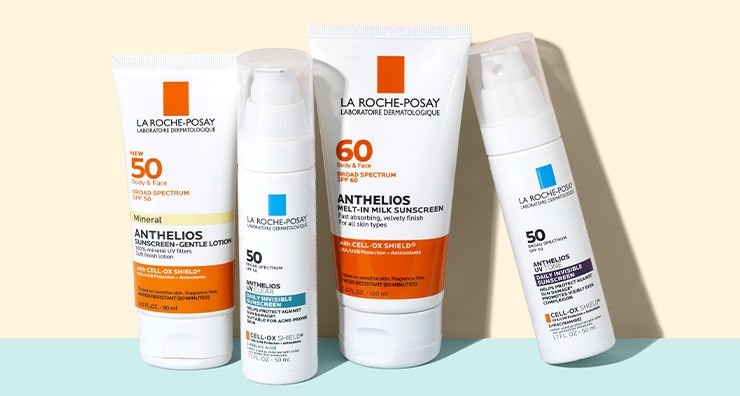 Four white containers of La Roche-Posay sunscreen standing up on a pastel blue surface in front of a cream background.