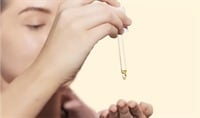 A woman with fair skin holds a dropper of Jurlique Rare Rose Facial Oil above her palm.