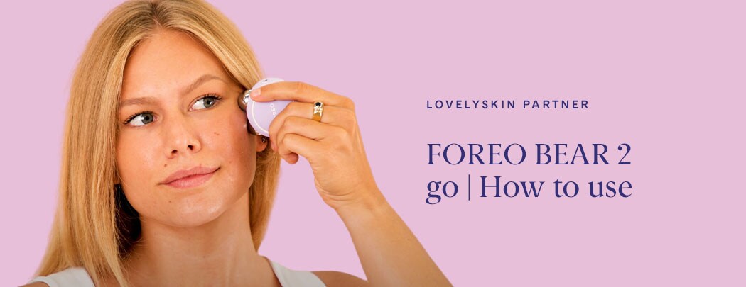 A woman with a light to medium skin tone and blonde hair presses a microcurrent device to her cheekbone.