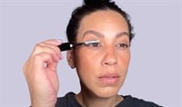 A woman looking to the side, applying white lash primer to her lashes.