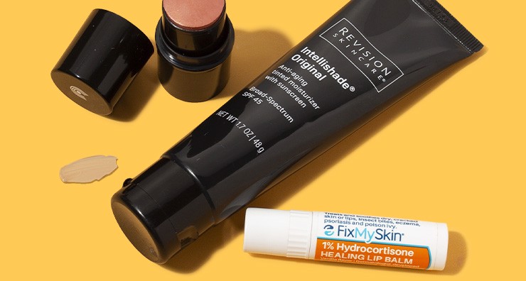 Tubes of FixMySkin lip balm, Revision Skincare Intellishade moisturizer and pink Dr. Hauschka lip and cheek tint on an orange background.