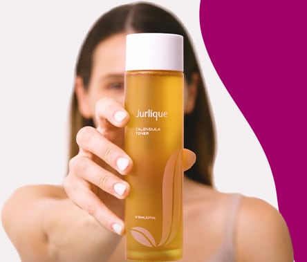 A woman with olive toned skin and brown hair holds a marigold-colored bottle of Jurlique Calendula Toner.