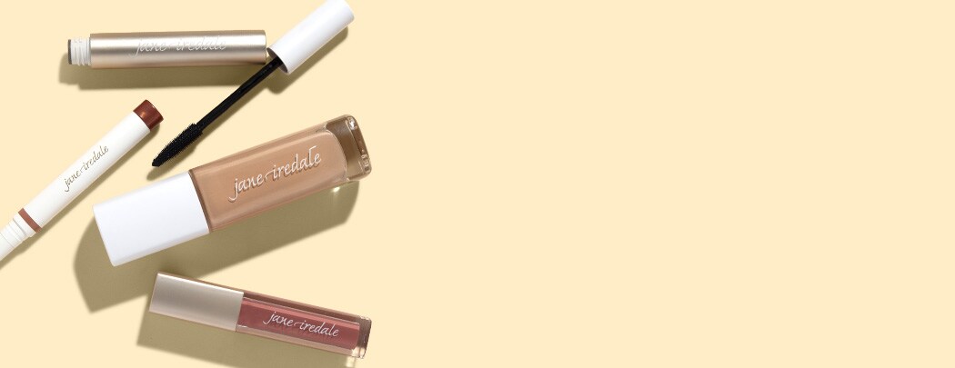 A gold mascara tube lays next to a white eyeshadow stick, a bottle of liquid foundation and a rose-colored lip gloss.