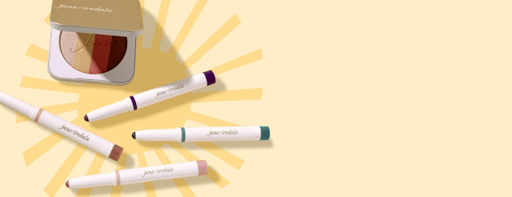 A gold compact with a multi-shade shimmer bronzer and four eyeshadow sticks in nude, purple and blue shades lay on a light yellow background.