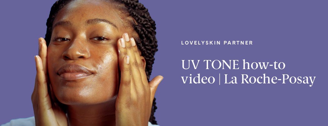 A woman with a deep skin tone and dark brown hair uses both hands to apply La Roche-Posay UV Tone Sunscreen to her face.