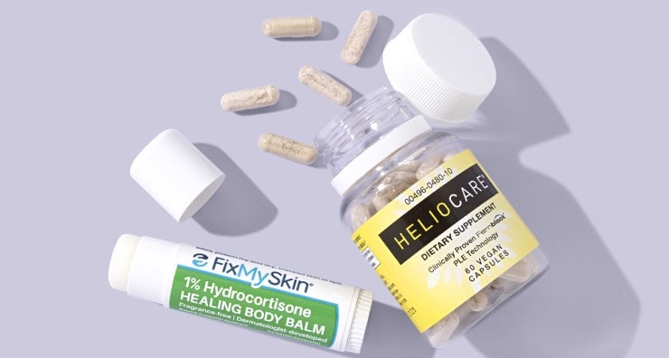 A tube of FixMySkin Healing Body Balm with the lid off and a bottle of Heliocare supplements with pills spilling out onto a lavender background.