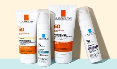 Four white containers of La Roche-Posay sunscreen standing up on a pastel blue surface in front of a cream background.