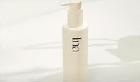 A cream colored pump bottle of Ina Balancing Cleanser sits on a white countertop with natural shadows behind it.