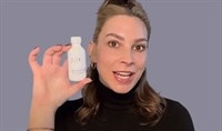 A woman looking forward with her mouth open holding a skin care bottle.