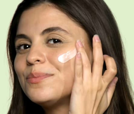 A woman with medium, olive-toned skin and medium brown hair applies Althaea Skin Day Serum to her cheek.