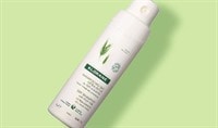 A bottle of Klorane dry shampoo on arranged on a green background.