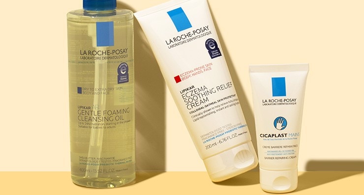 Containers of three La Roche-Posay Lipikar products, including a cleansing oil, moisturizer and hand cream, on an off-white background.