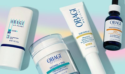 Four products lay over a blue background with a rainbow hue. There is a treatment, a cream, a sunscreen and a serum.