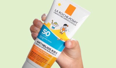 A hand with a medium skin tone holds a bottle of La Roche-Posay Anthelios Kids Gentle Lotion Sunscreen SPF 50