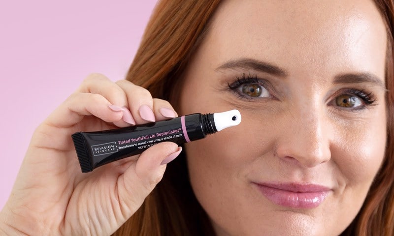 Woman holding tube of tinted lip replenisher