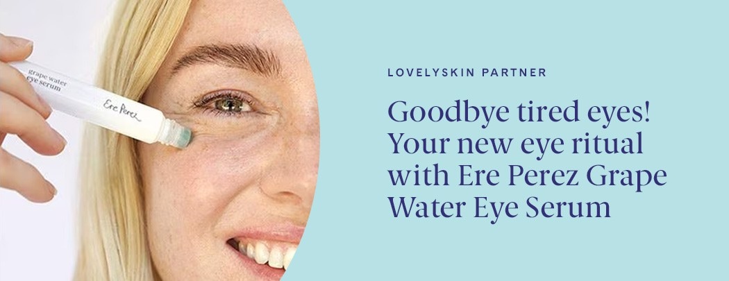 A woman with fair skin and blonde hair presses the Ere Perez Grape Water Eye Serum to her skin while smiling.
