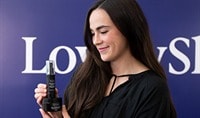 A woman with a light skin tone and dark hair holds Advanced Pigment Corrector+ and Tone+ Correcting Pads while smiling softly.