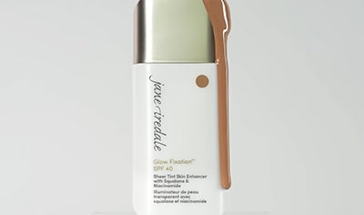 A bottle of Jane Iredale Glow Fixation SPF 40 sits with product dripping over it.