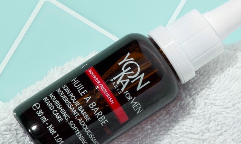 Yon-Ka Paris Men's Beard Nourishing Oil laying on a white washcloth and blue bathroom tile
