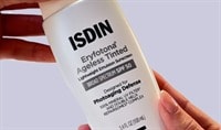 A person holds a bottle of ISDIN Eryfotona Ageless Tinted Lightweight Emulsion Sunscreen SPF 50 New Formula in both hands.