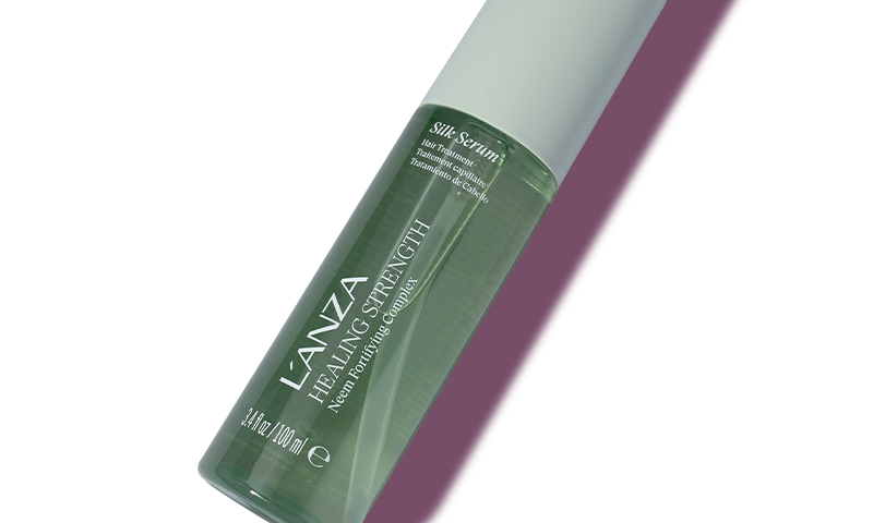 A green bottle of L'ANZA Healing Strength Neem Plant Silk Serum on a soft pink background