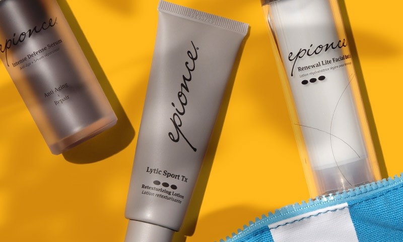 Sunlit Epionce products with natural leaf shadows, spilling out of a blue and white striped cosmetic bag