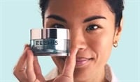 An asian woman smiling and holding a jar of ELEMIS Overnight Matrix over her face.