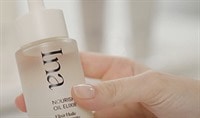 A person with fair skin and polished nails holds a bottle of Ina Nourishing Oil Elixir.