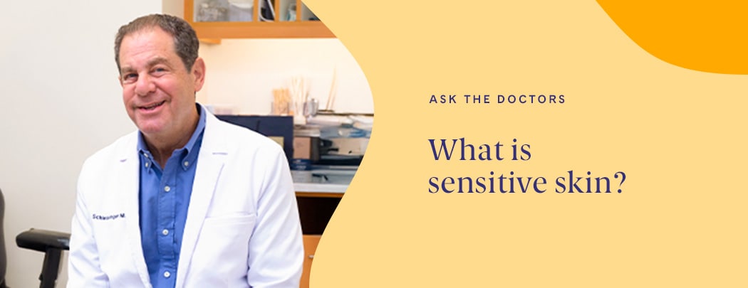 Dr. Joel Schlessinger, a board-certified dermatologist, sits in a patient room in a white jacket as he smiles.