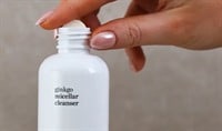 A person with a medium skin tone and chrome pink nails adds an Ere Perez Ginkgo Micellar Cleanser tablet to the white bottle.