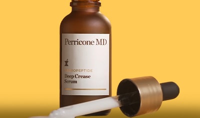 A brown bottle of Perricone MD Neuropeptide Deep Crease Serum sits on clear glass. The dropper is laying next to the bottle with product dispensing.