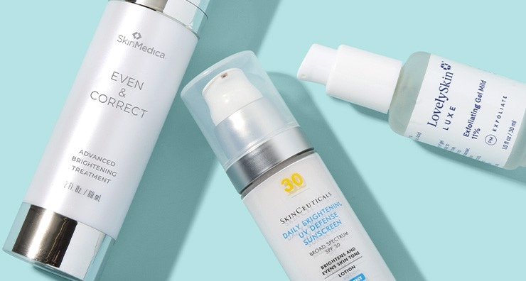 Bottles of SkinMedica Even & Correct serum, SkinCeuticals sunscreen and LovelySkin Exfoliating Gel on a light blue background.