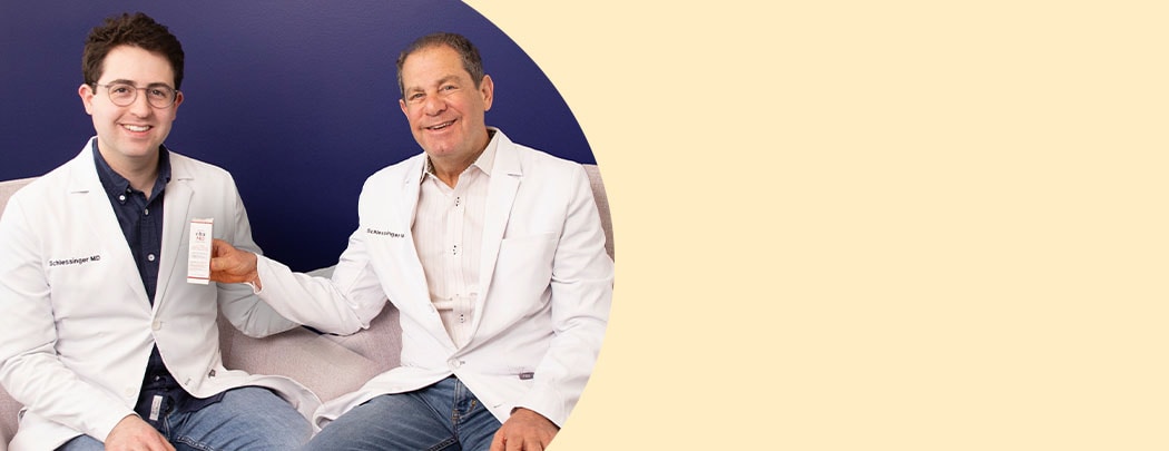 Drs. Joel and Daniel Schlessinger sit next to one another while smiling. Dr. Joel holds a box of EltaMD UV Clear Blemish-Prone & Oil Balancing SPF 50.