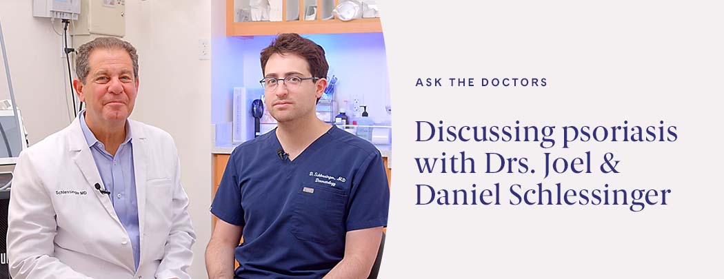 Two dermatologists, one in a white jacket and one in scrubs, sit next to one another in a patient room smiling.
