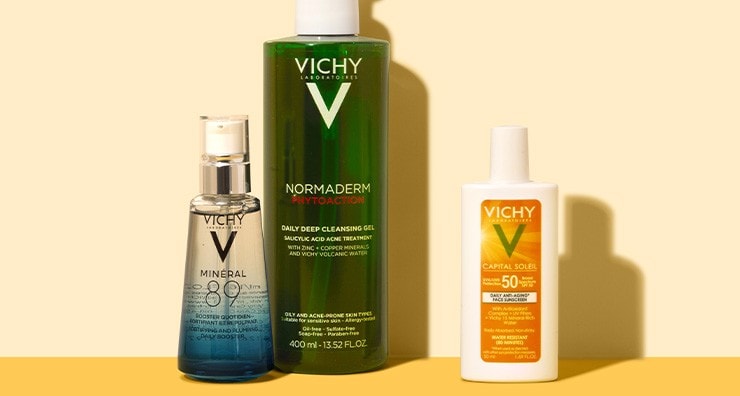 Three Vichy skin care bottles standing up on a yellow background.