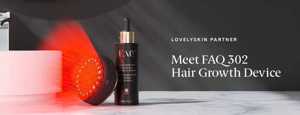 A black, circular device faces outward with a ring of red lights shining. It leans against a black serum bottle with gold details.