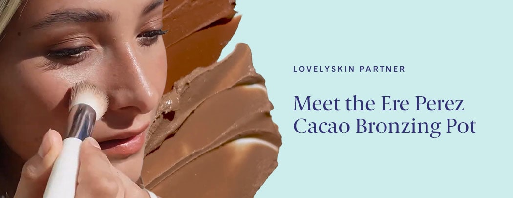 A woman with a light skin tone and blonde hair presses a brush to her cheek. There are swatches of the Ere Perez Cacao Bronzing Pot behind her.