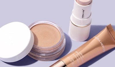 Ere Perez highlighter pot, jane iredale highlighter stick and Laura Mercier liquid highlighter on a lavender background