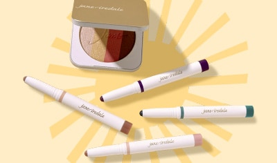 A gold compact with a multi-shade shimmer bronzer and four eyeshadow sticks in nude, purple and blue shades lay on a light yellow background.