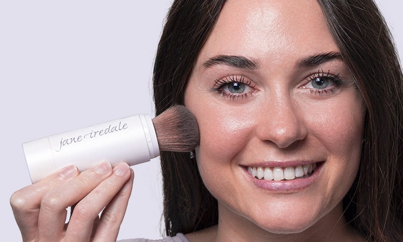 Woman smiling and applying Jane Iredale sun protection
